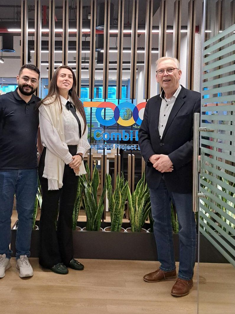 Three people standing in front of the Combi Lift MEA office entrance, smiling for the camera.