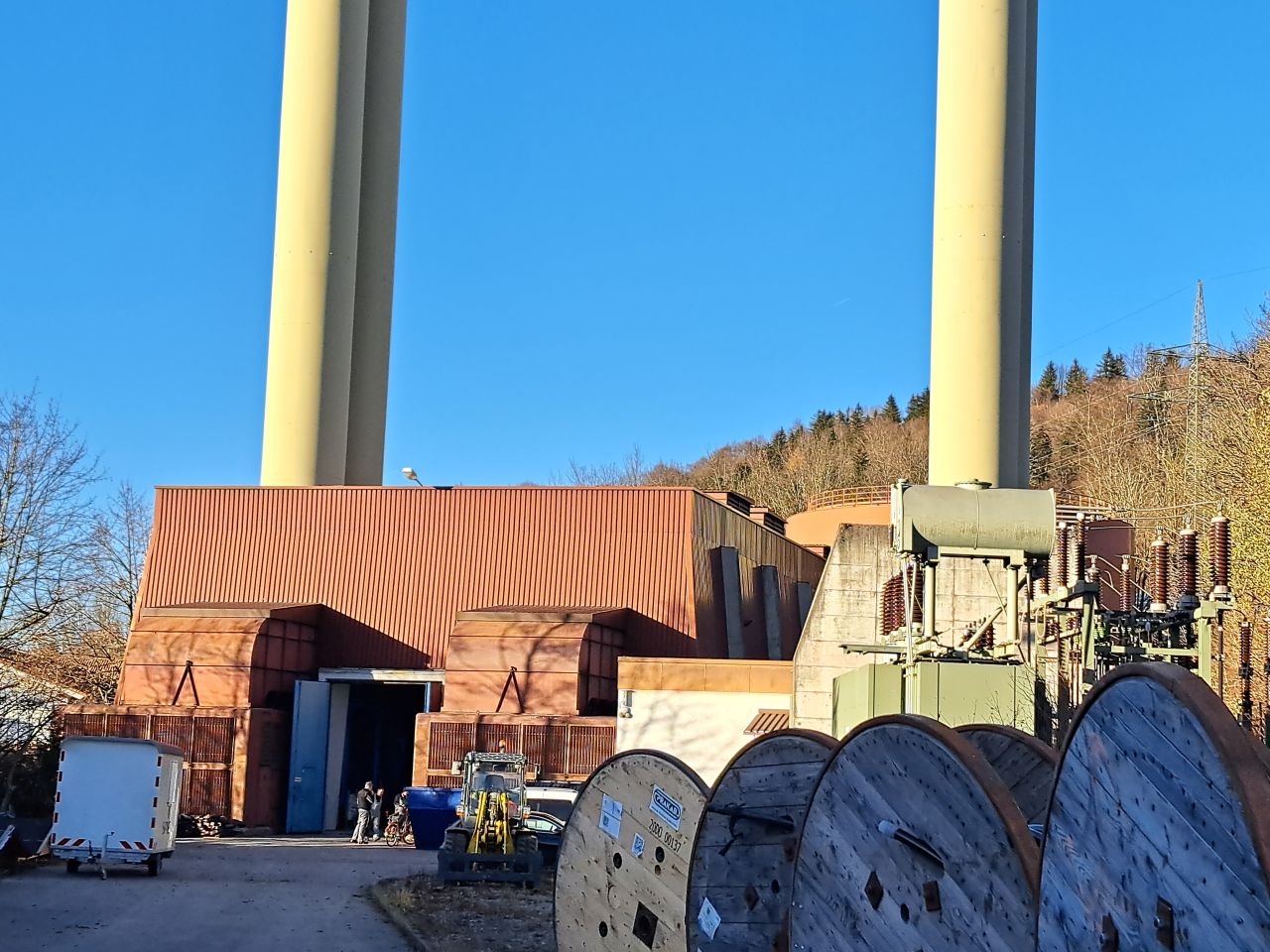 Exterior view of the brown-clad Hausham power plant with tall chimneys under a clear blue sky.
